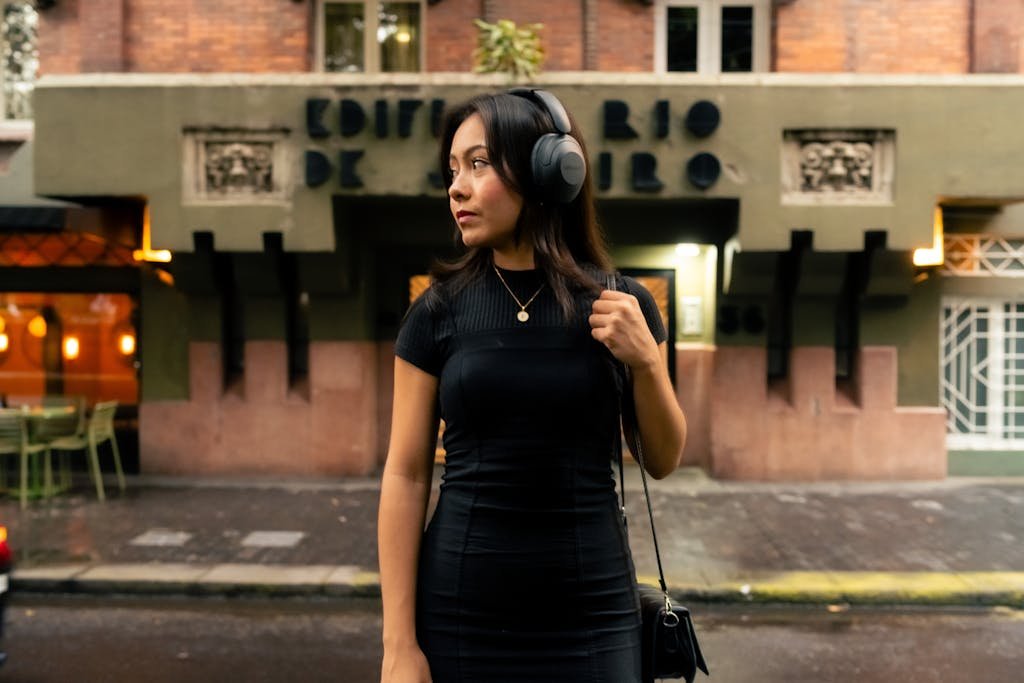 Young woman wearing headphones walks past a historical building on a city street.