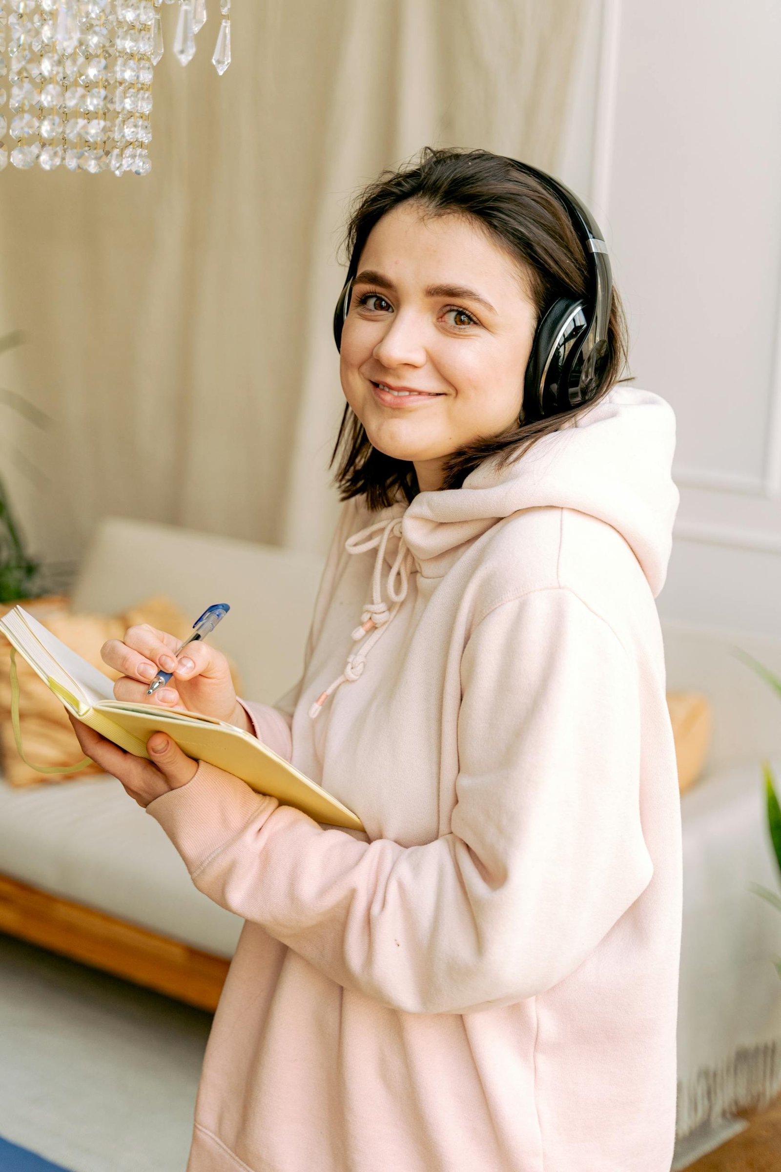 Young woman with headphones, writing notes in a cozy indoor setting.